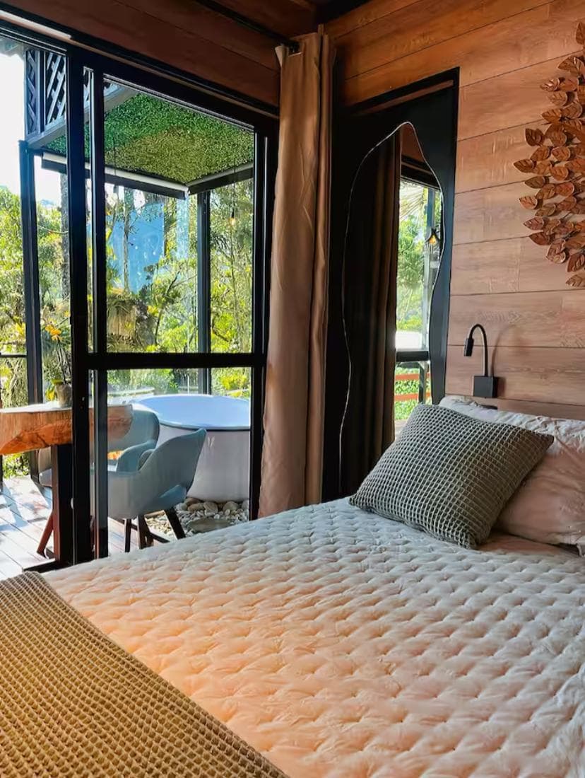 Cama de casal com vista, pelas portas de vidro, para a banheira no deck e a mata
