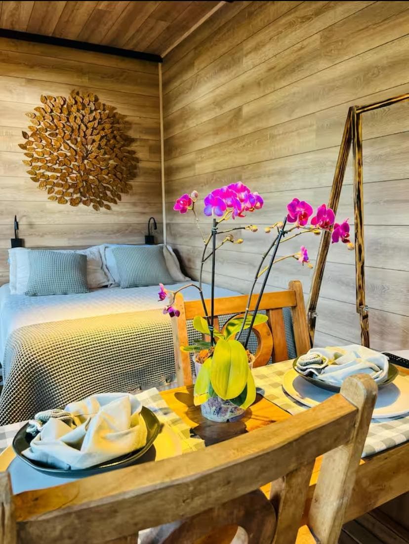 Quarto revestido em madeira com cama de casal e mesa posta com orquídea