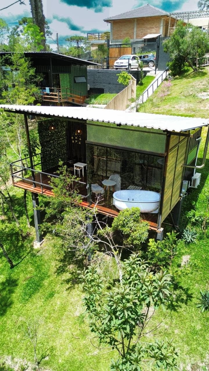 Vista do alto da cabana suspensa, com a frente de vidro e o deck cercados de vegetação